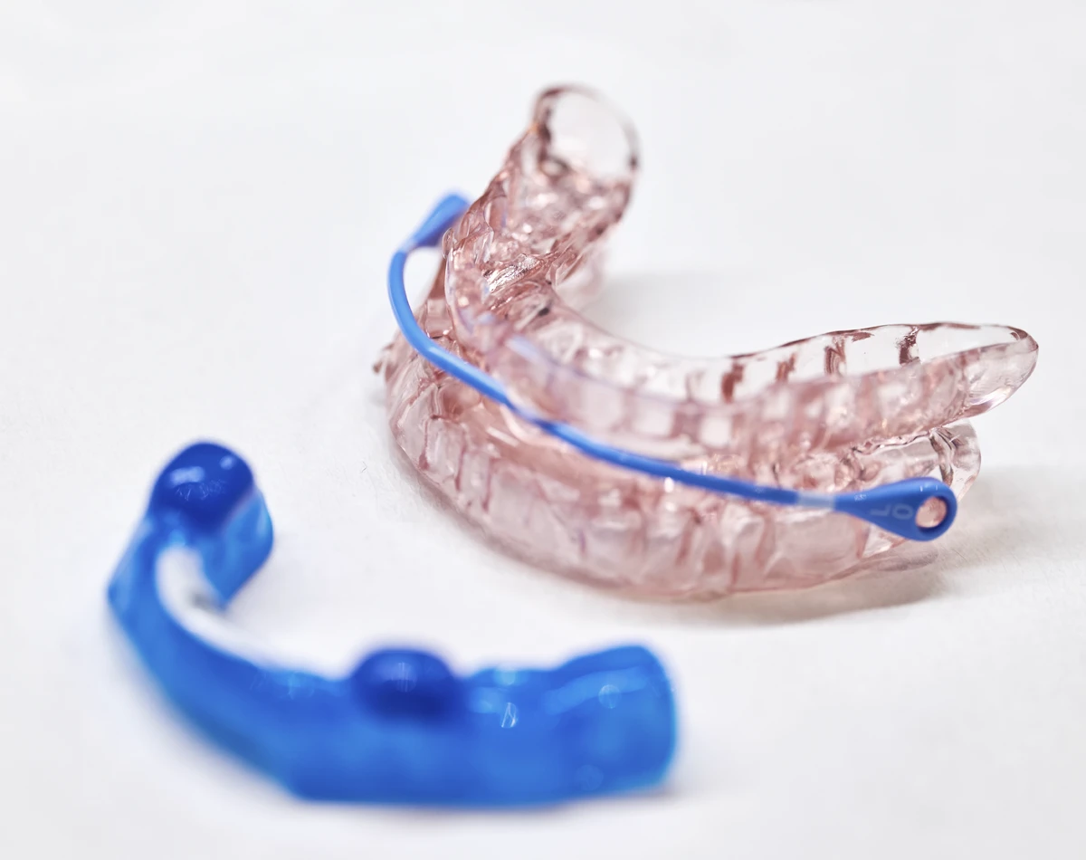 Transparente Schnarchschiene in Pink und blauer Halterung auf weißem Hintergrund.